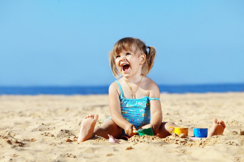 Девочка сидит в песке и смеется
