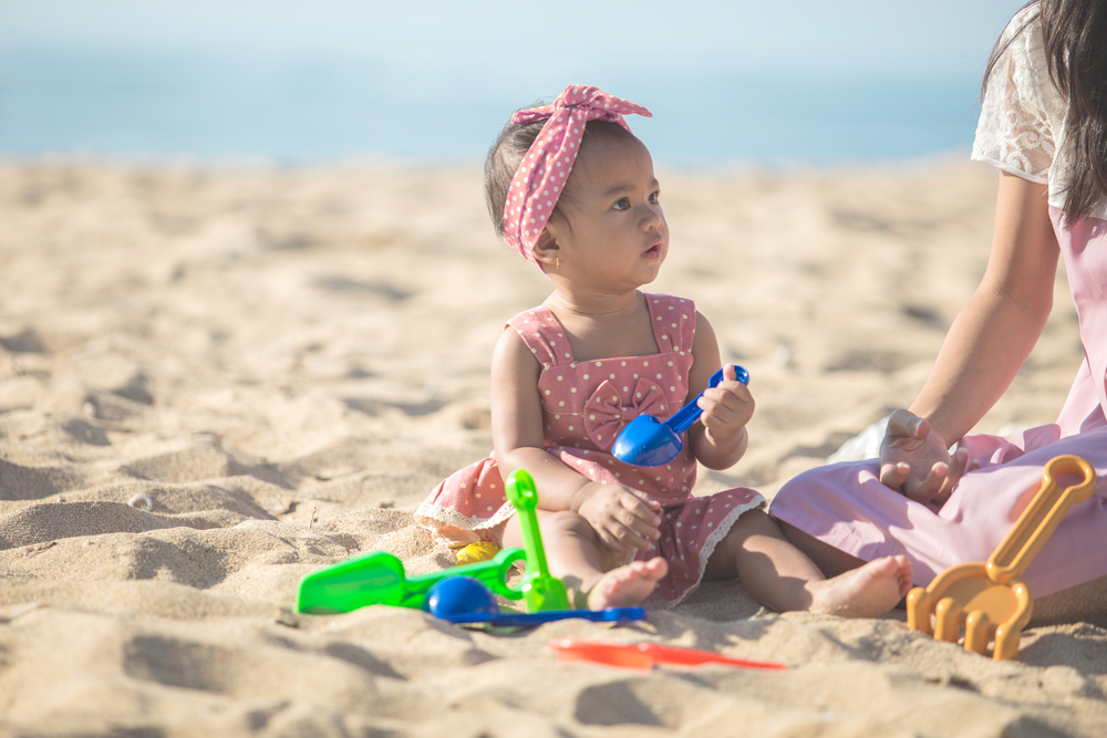 Девочка с мамой на пляже роется в песке