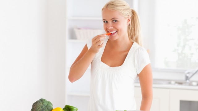 Жінка їсть овочі на кухні