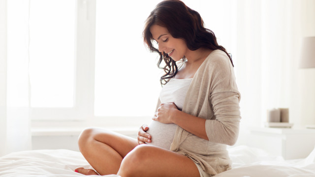 Вагітна брюнетка сидить на ліжку